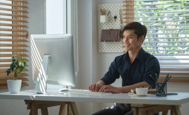 Parlak ev ofisinde modern bilgisayarla çalışan yakışıklı bir iş adamı..