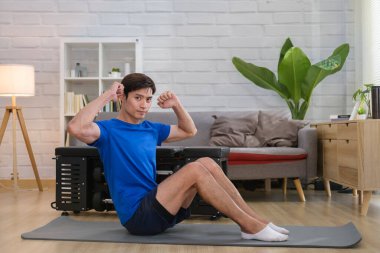 Genç adam oturma odasında egzersiz yapmadan önce vücudunu esnetiyor..