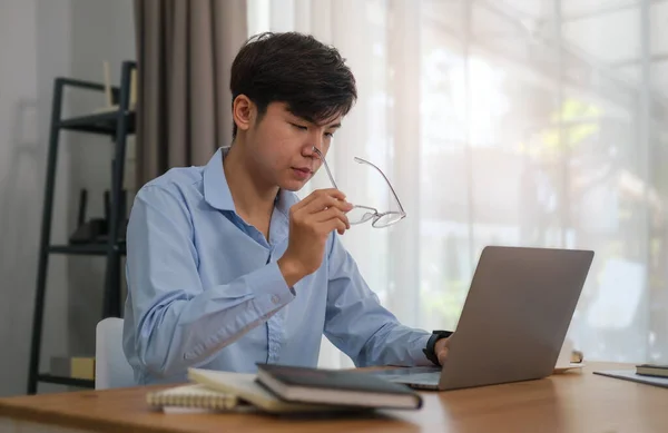 漂亮的亚洲男性自由职业者举着眼镜 在明亮的办公室里使用笔记本电脑 — 图库照片