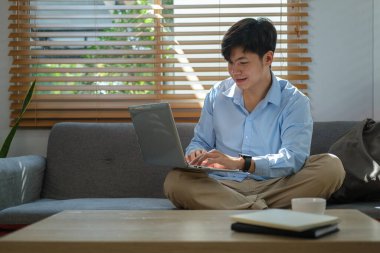 Man in casual clothes surfing internet, working online with laptop computer while sitting on couch at home.	