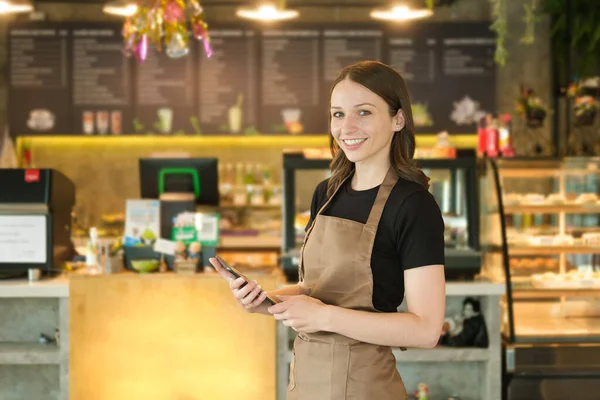 Portrait of young entrepreneur of coffee shop standing in front of counter at her trendy cafe.