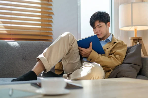 Genç Adam Rahat Bir Kanepeye Uzanıp Kitap Okuyor — Stok fotoğraf