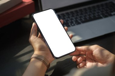 İş yerinde otururken akıllı telefonu tutan kadının omuz üstü görüntüsü..