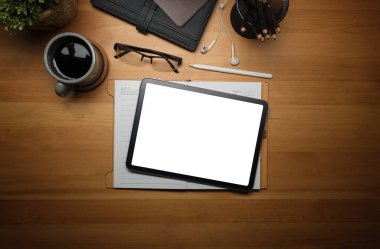 Flat lat digital tablet with blank display, coffee cup, stationery and houseplant on wooden table.