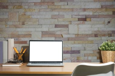 Dizüstü bilgisayarı, kitapları, kalem tutacağı ve ahşap masadaki bitki örtüsüyle rahat çalışma alanının ön görüntüsü.