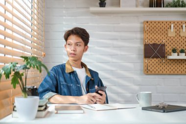 Düşünceli Asyalı erkek serbest çalışan ofiste oturuyor ve pencereden dışarı bakıyor..