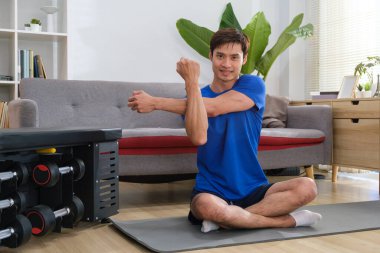 Spor elbiseli yakışıklı Asyalı adam ev antrenmanı sırasında kollarını esnetiyor. Fitness, spor ve sağlıklı yaşam tarzı kavramı.