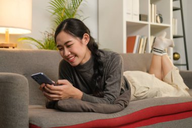 Hoş, genç bir kadın rahat koltukta dinleniyor, sosyal ağlarda akıllı telefondan sohbet ediyor..