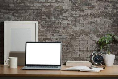 Boş ekranlı dizüstü bilgisayar, beyaz boş çerçeve, ahşap masa üzerinde kitaplar ve saksı bitkisi..