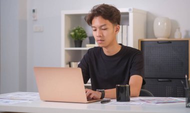 Dizüstü bilgisayarda çalışan genç bir erkek web sitesi tasarımcısı. Ofiste cep telefonu için başvuru planlıyor. Kullanıcı deneyimi kavramı.