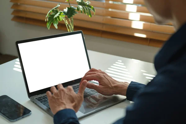 View over businessman shoulder hands typing on keyboard of laptop computer at office desk.