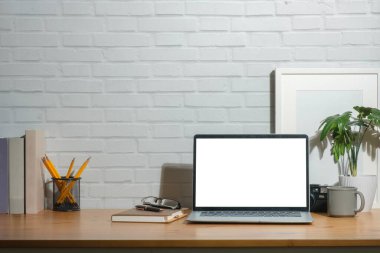 Boş ekran, resim çerçevesi ve ahşap çalışma masasında kırtasiye malzemesi olan dizüstü bilgisayarın ön görüntüsü.