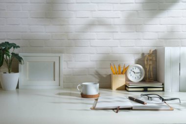 Beyaz boş çerçeve, çalışma masasında kahve fincanı, defter ve saksı bitkisi oluşturur..