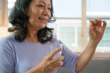 Gülümseyen orta yaşlı kadın elinde hap ve bir bardak su tutuyor. İlaç, tedavi ve sağlık hizmetleri kavramı.