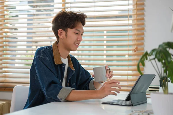 快乐的亚洲男性自由职业者在家喝咖啡和上网玩数码平板电脑 — 图库照片