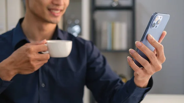 Smiling businessman drinking coffee and chatting or typing text message on smartphone.
