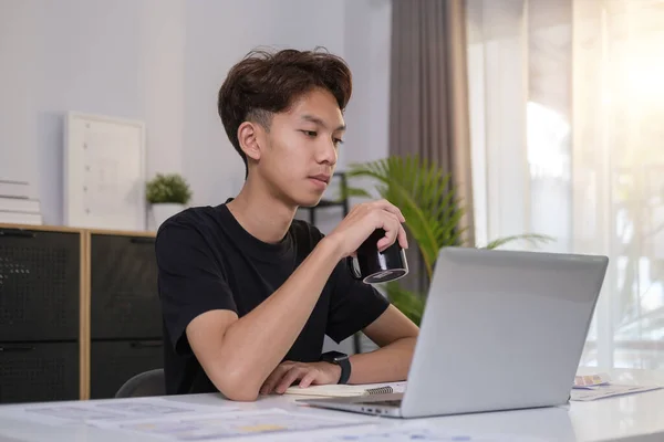 亚洲年轻人喝热咖啡 阅读电子邮件或在笔记本电脑上上网工作的照片 — 图库照片