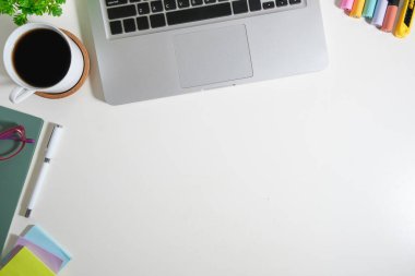 Dizüstü bilgisayarı ve çeşitli ofis malzemeleri olan beyaz çalışma masasının üst görüntüsü. Metnin için boşluk kopyala.