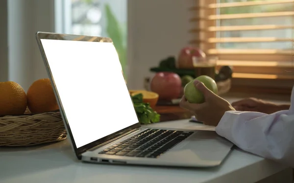 女性营养师拿着一个绿色苹果 在办公室用笔记本电脑工作的剪影 — 图库照片
