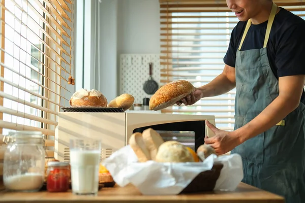Man removing freshly baked bread from oven in kitchen.