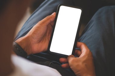 Over shoulder view of young man holding smart phone with blank screen.	