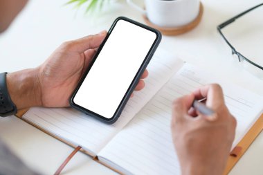 Beyaz ekranlı, akıllı telefonu tutan ve not defterine not alan..