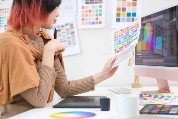 Asian female interior designer choosing color from samples for home interior design project in modern studio.