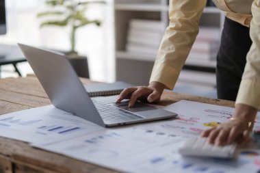 Bilgisayarı kullanan tanınmayan analist, satış istatistiklerini analiz ediyor, masadaki mali veri belgelerini inceliyor..