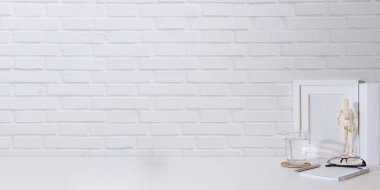 Kitapların, bir bardak suyun ve beyaz masanın üzerinde gözlüklerin olduğu küçük bir iş yeri. Metnin için boşluk kopyala.