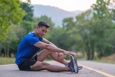 Spor elbiseli bir adam parkta antrenmandan önce bacaklarını açıyor, ısınıyor..