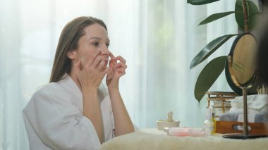 Caucasian woman in bathrobe applying sheet mask on her face. Beauty routine, self care concept.	