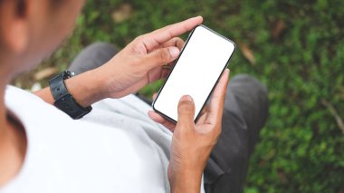 Over shoulder view of young man holding smart phone with blank screen.	