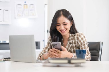 Ofiste akıllı telefon kullanan genç bir kadın tasarımcının portresi. Teknoloji ve kullanıcı arayüzü tasarımı kavramı