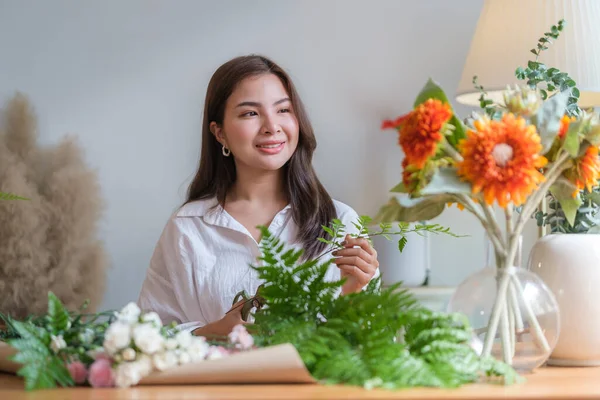 Positive female florist creating beautiful bouquet of colorful different flowers in modern interior floral shop.