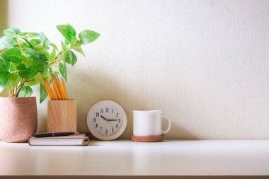 Bir fincan kahve, saat, saksı ve kalem tutacağı olan ofis masası..