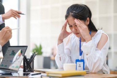 Stresli kadın ofis çalışanı, masa başında oturmuş el ele tutuşurken üzgün, endişeli, yorgun ve bunalmış hissediyor..