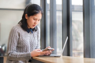 Modern kahve dükkanında dizüstü bilgisayarı olan ve akıllı telefon kullanan bir kadın..