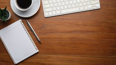 Kablosuz klavyesi, not defteri ve ahşap masasında kahvesi olan basit bir iş yeri manzarası..