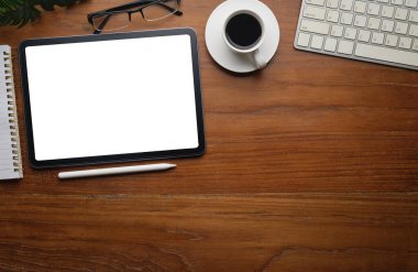 Düz yatış, beyaz ekranlı dijital tabletin üst görüntüsü, kahve fincanı, bardak ve not defteri ahşap çalışma masasında..