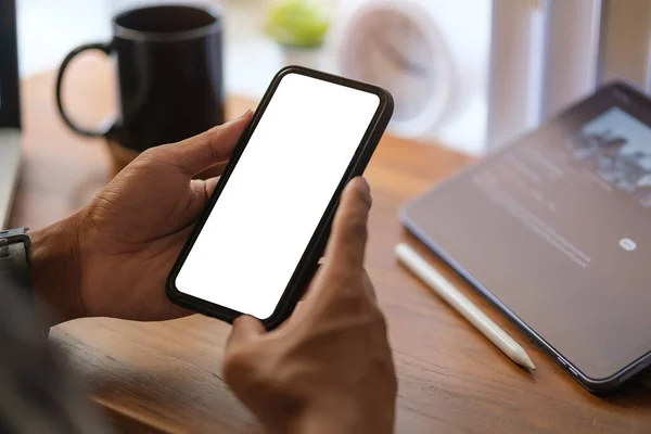 stock image Creative man hand holding smartphone with white empty screen at wooden working desk.