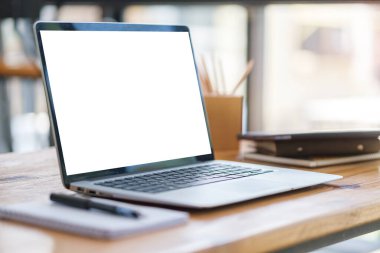 Beyaz ekranlı dizüstü bilgisayar, tahta ofis masasında defter ve kalem tutacağı..