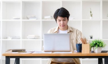 Çağdaş ofiste dizüstü bilgisayarda çalışan yakışıklı Asyalı genç adam..