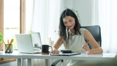 Attractive businesswoman using laptop computer and checking financial reports on white office desk.	