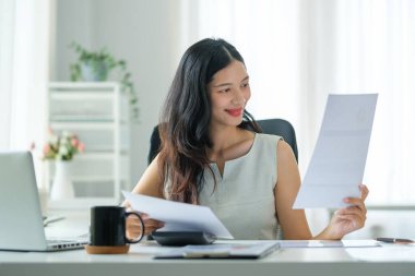 İş kadını ofis masasında oturuyor ve iş belgelerini kontrol ediyor..