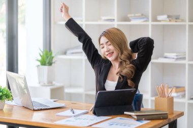 Happy female employee stretching her arms in the air, relaxing at workplace.