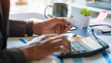 Genç Asyalı adam kredi kartı tutuyor ve hesap makinesi kullanıyor. Çevrimiçi alışveriş, e-ticaret, internet bankacılığı kavramı.
