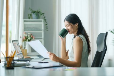 Pleasant young woman enjoying her morning coffee while sitting at her workplace.