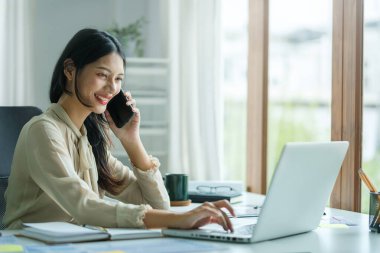 Young asian woman talking on mobile phone and working online with laptop computer at outdoor.	
