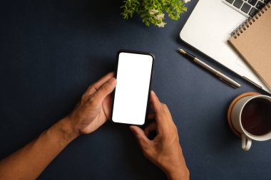 Bir adamın elinin yukarıdan görünüşü ve masadaki akıllı telefonu boş ekran tutuşu.