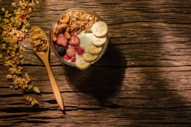 Sağlıklı kahvaltı. Yoğurtlu granola, böğürtlen ve muz güneş ışığıyla aydınlatılmış ahşap bir masada..